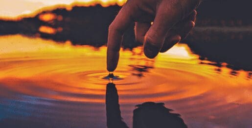 a finger ripples water in a pond at sunset