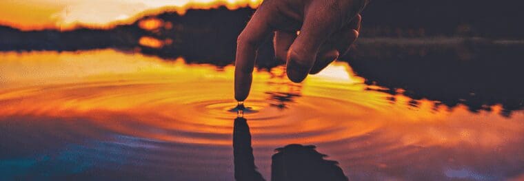 a finger ripples water in a pond at sunset