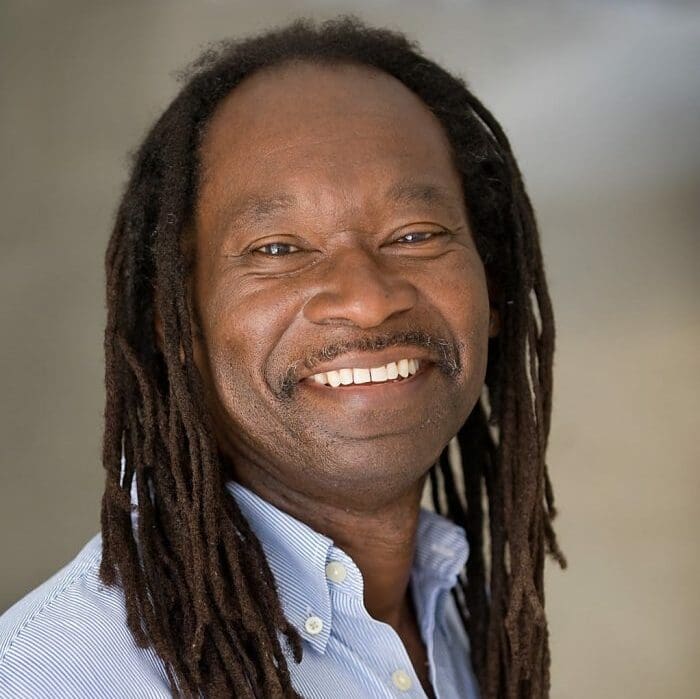 Anand Prahlad, a Black man with long dreadlocks, looks directly at the camera with a big smile on his face.