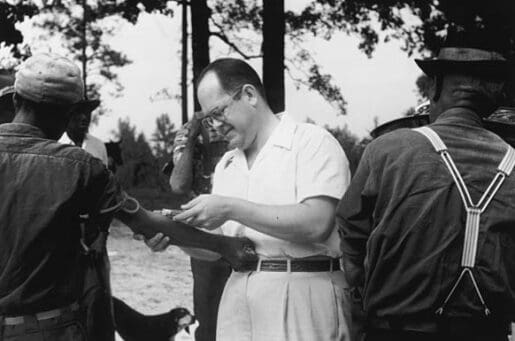 white man taking blood sample from black man's arm to test for Syphilis , part of the Tuskegee study.