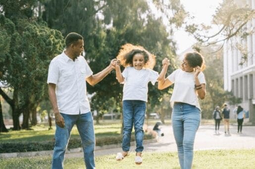 family of color in white shirts and blue jeans playing in a park