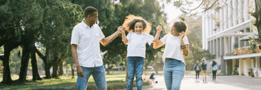 family of color in white shirts and blue jeans playing in a park