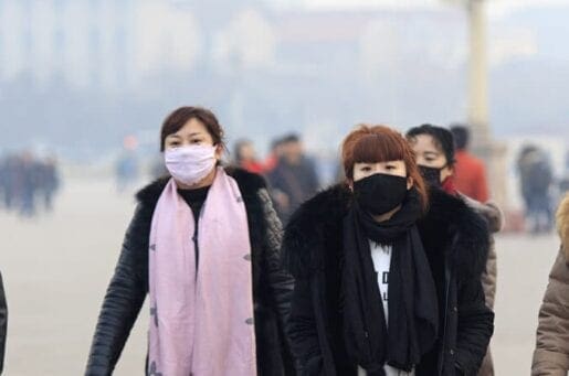 two people in masks and heavy winter coats walking through busy streets