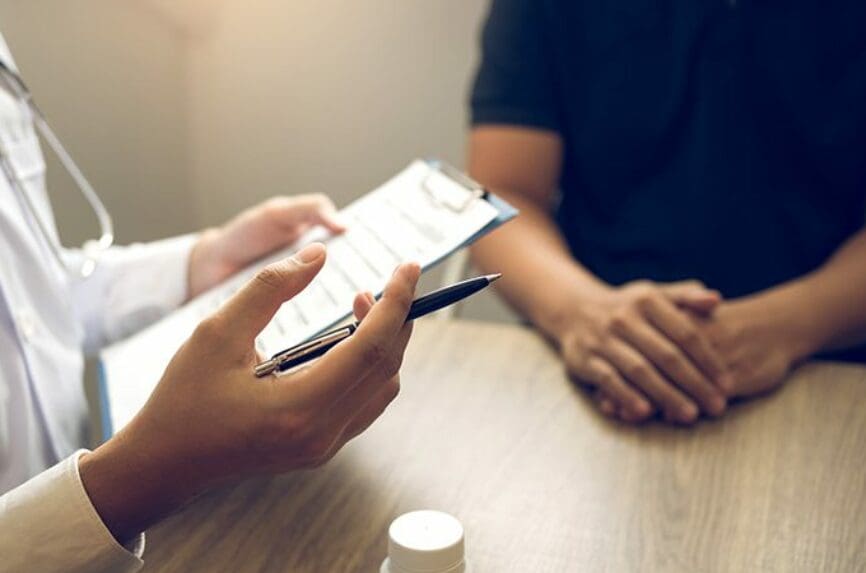 doctor holding prescription pad with pen in hand talking to a man in a blue shirt