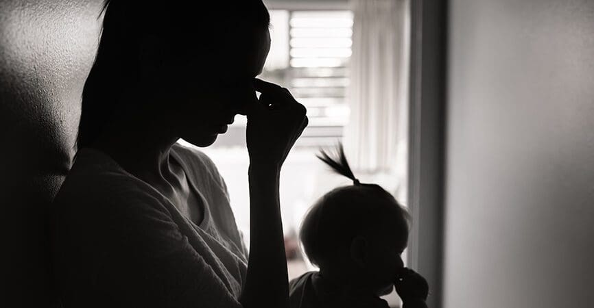 silhouette of a woman with her head in her hands and a baby in her lap