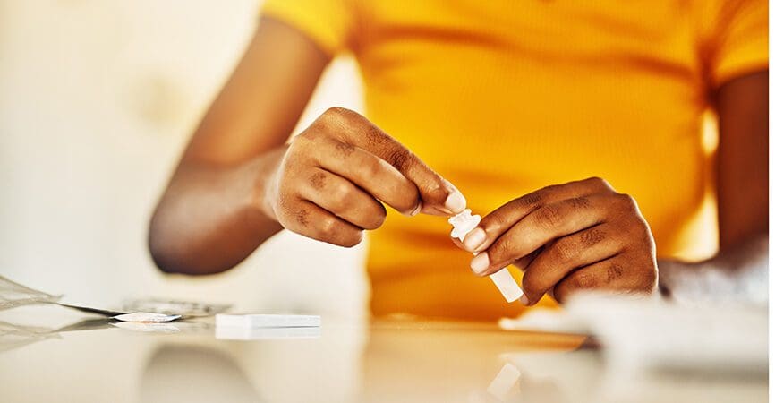 Hands of African female with HIV and Aids at home blood self test kit sitting at a desk waiting to check for results. Closeup of young afro woman with medicine or pills for a medical condition.