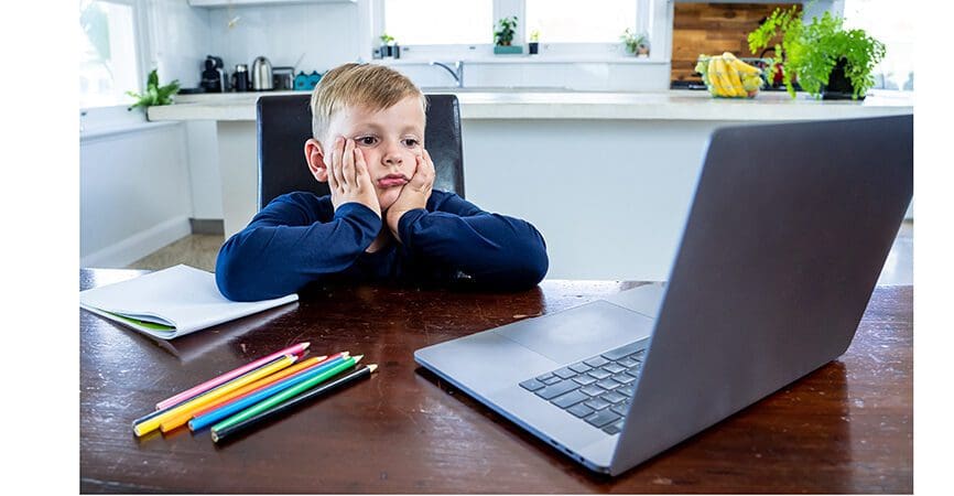 Coronavirus Outbreak. Lockdown and school closures. School boy with face mask watching online education classes feeling bored and depressed at home. COVID-19 pandemic forces children online learning.