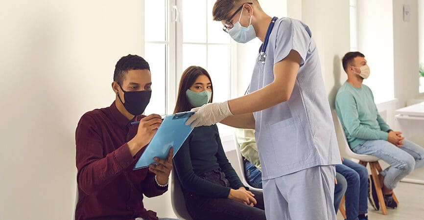 Diverse people signing papers while waiting in line to get influenza or coronavirus shots at the hospital or medical center. African-American man putting signature on Informed Consent for Vaccination