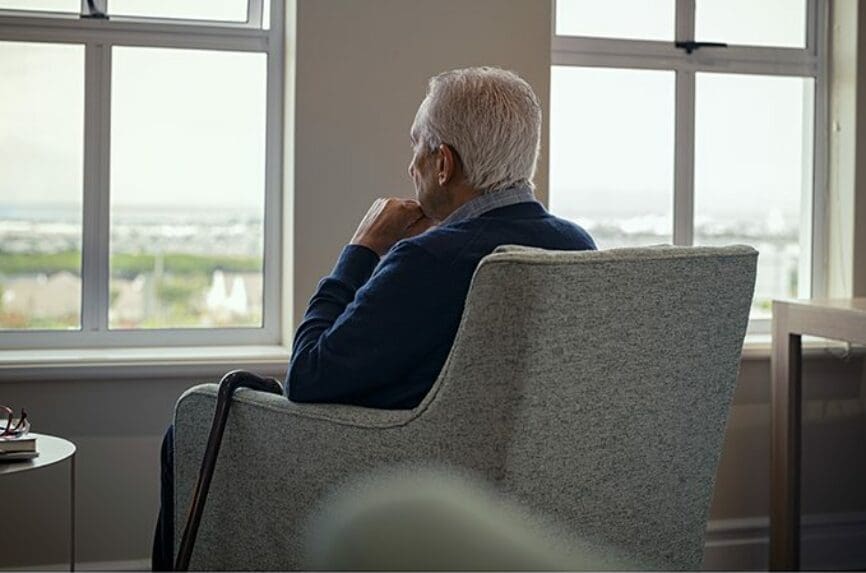 Rear view of senior man sitting on armchair and looking through the window. Lonely old man sitting at home near window during covid19 outbreak. Thoughtful retired man abandoned at nursing home.