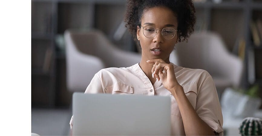 Thoughtful young African American woman in glasses look at laptop screen work online at home office. Pensive ethnic female use computer distant think ponder of problem solution. Technology concept.