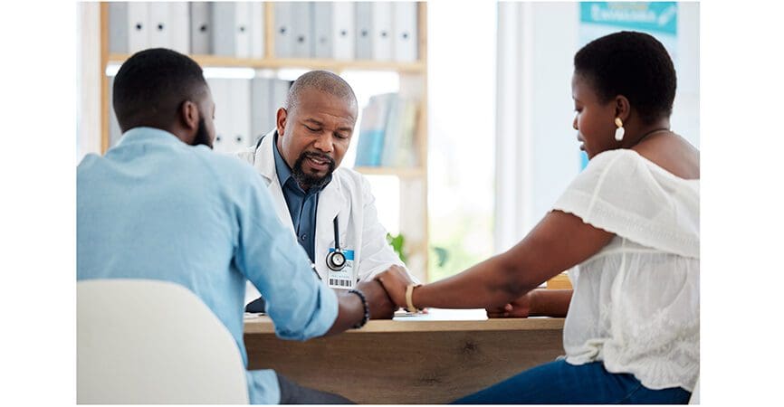 Doctor, black couple and holding hands in consultation clinic, support and comfort. Healthcare, obstetrician and man and woman talking with medical professional for advice, fertility treatment or ivf