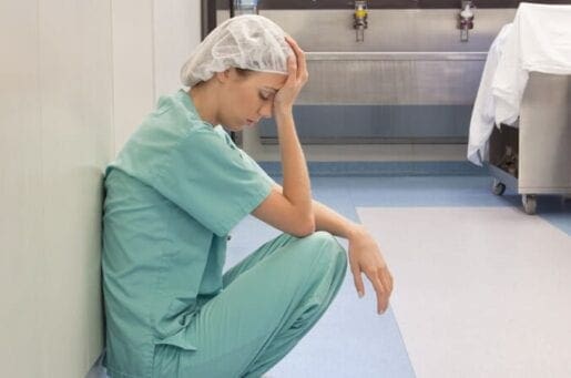 woman in scrubs leaning crouched against a wall