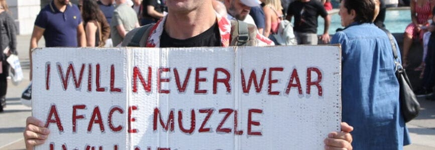 white man holding a white sign stating in red lettering 