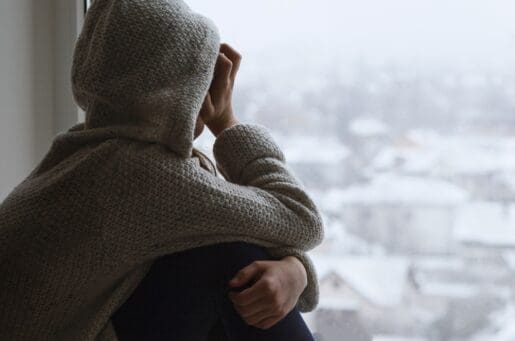 depressed teen in hooded short looking out window