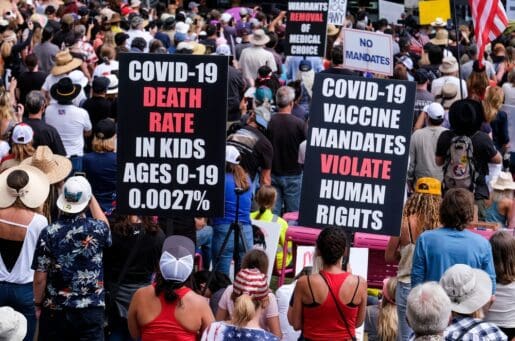 large crowd of protesters, one very large black sign stating "Covid-19 death rate in kids ages 0-10 is 0.0021%" in white lettering