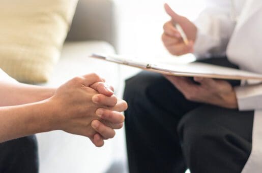 clasped hands of patient, doctor's hands with pen and clipboard