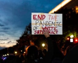 man of color holding a white sign stating "end the pandemic of white supremacy"