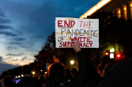 man of color holding a white sign stating "end the pandemic of white supremacy"